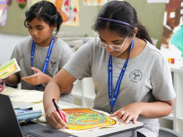 Two students at AKA Dhaka focused on painting and colouring artwork during art class.